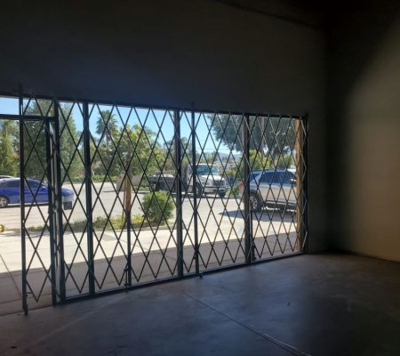 An empty room features a metal gate with a parked car in front, creating a stark and industrial atmosphere.