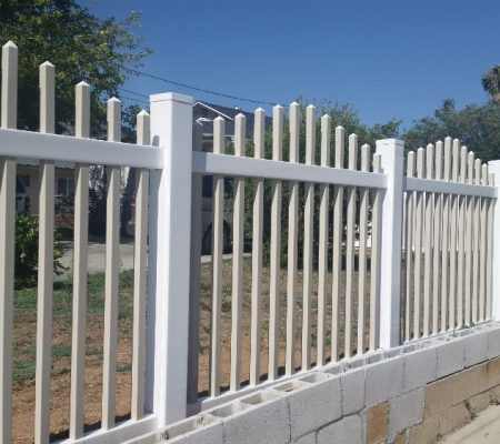 A white fence runs alongside a concrete sidewalk, creating a clear boundary between the path and adjacent area.