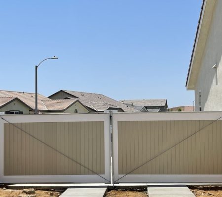 Double beige and white gated fence in a suburban backyard with houses and clear blue sky in the background.