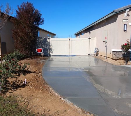 A driveway featuring a concrete walkway alongside a fence, creating a clear path to the entrance.