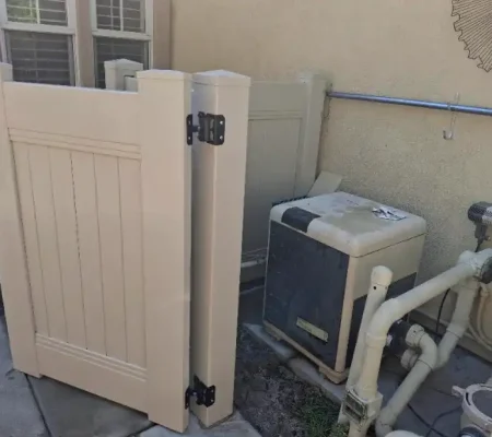 A house with a white door and beige gate, featuring two air conditioning units and two pipes with black handles on a concrete ground.