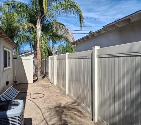 Residential area with a gray metal fence, white air conditioner, pool heater, and a palm tree under a clear blue sky.