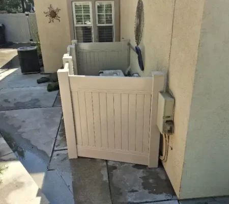 Residential area with a white gate, open door, and wet ground, featuring two windows, trash cans, and a star decoration.