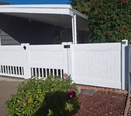 A white wooden fence with a gray roof, surrounded by a porch, in front of a house with a gray roof and white railing.