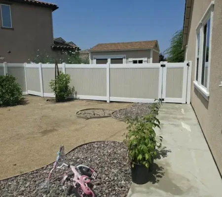 A serene backyard scene featuring a white picket fence, a concrete patio surrounded by colorful plants and a pink toy, and a house with a window and door.